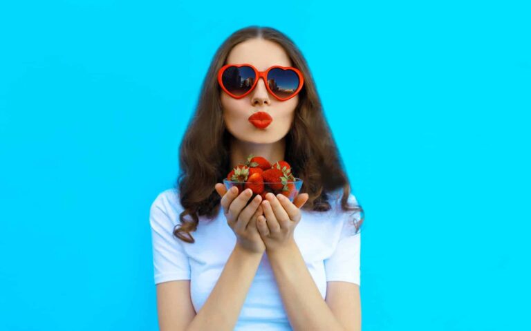 A young woman wearing sunglasses holds fresh berries in her palms, aware of the benefits antioxidants have for skin aging.