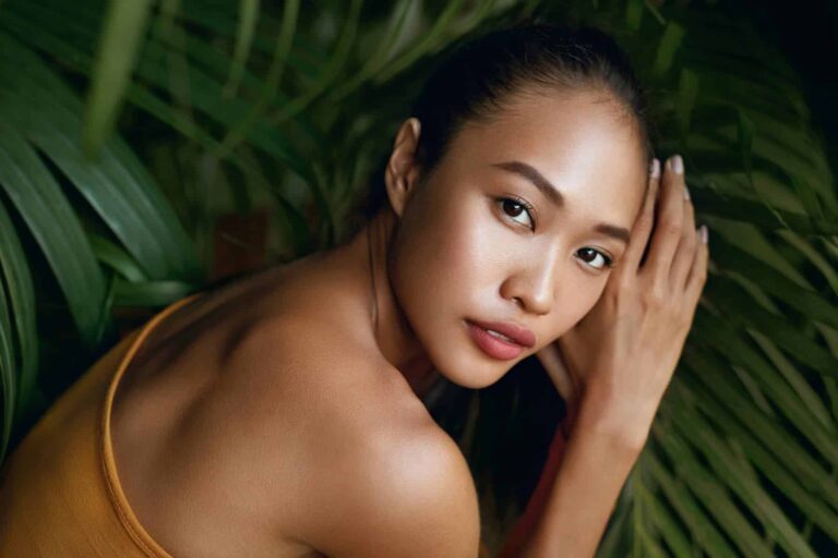 A woman model with natural makeup in a tropical setting, highlighting the benefits of vitamin E for healthy skin.