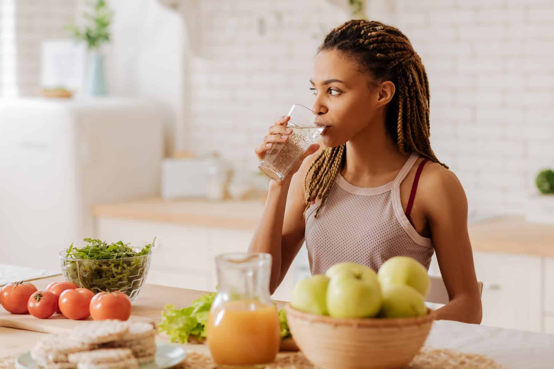 Slim and fit woman drinking water before having breakfast has healthy collagen boosting foods infront of her.
