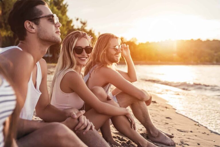 A confident woman sitting with friends on the beach at sunset, radiating positive energy and showing how to be attractive naturally.