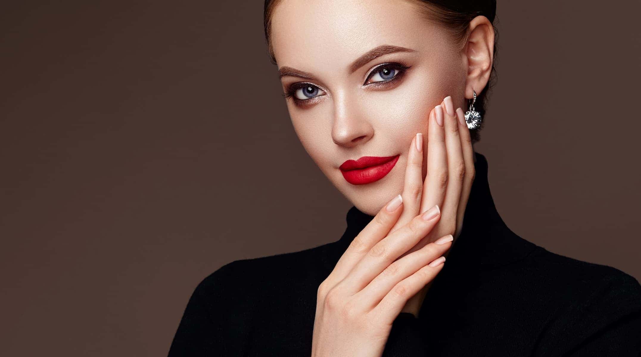 A close-up of a woman with makeup, her hand resting on her face, showing off her strong, healthy nails.