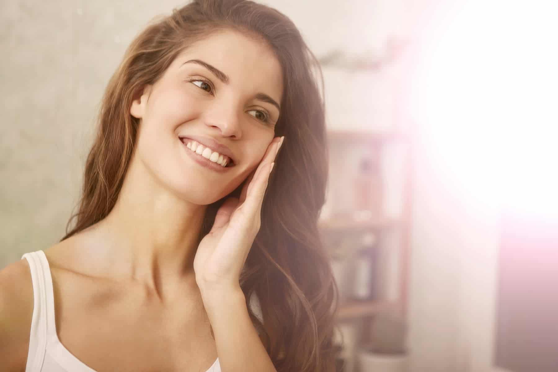 Smiling softly, a woman touches her face, pleased with the results she's seeing from adding collagen peptides to her diet.