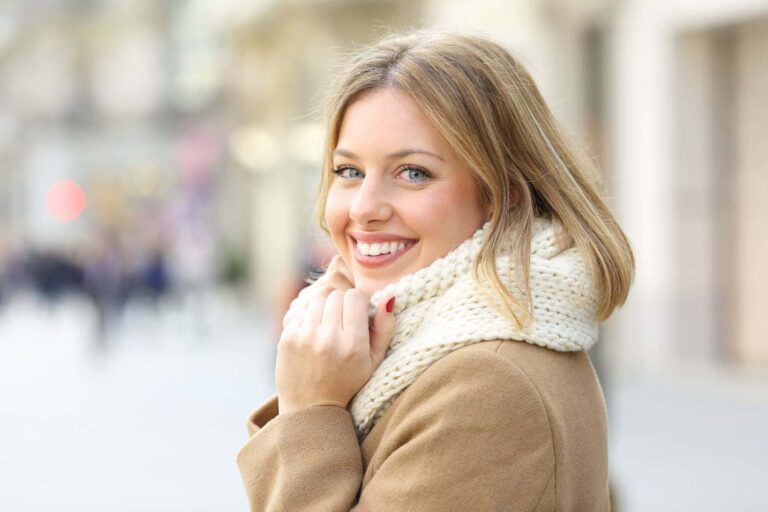 A smiling woman walking outdoors, holding her scarf, showing the results of learning how to build confidence in minutes.