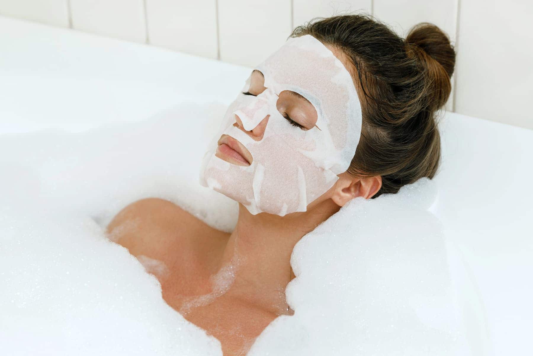 A woman relaxes in a bubble bath while wearing a collagen mask, enjoying a soothing skincare moment.