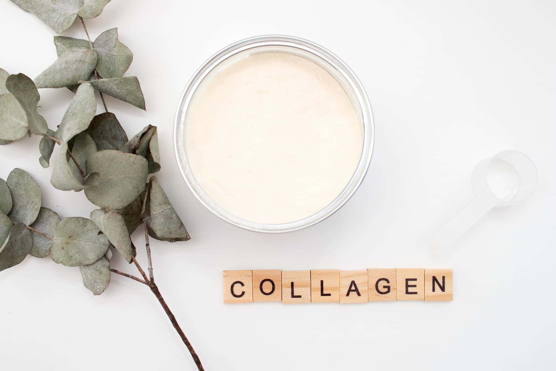 Wooden letter tiles spelling COLLAGEN sit beside a bowl and spoon filled with collagen powder, creating a clean and natural wellness aesthetic.