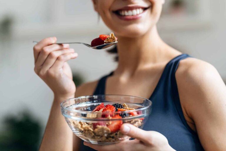 A woman eats a bowl of cereal topped with strawberries and blackberries, highlighting antioxidant-rich foods for clear skin.