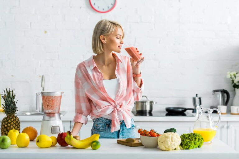A tall and slim woman drinks smoothie in her kitchen.