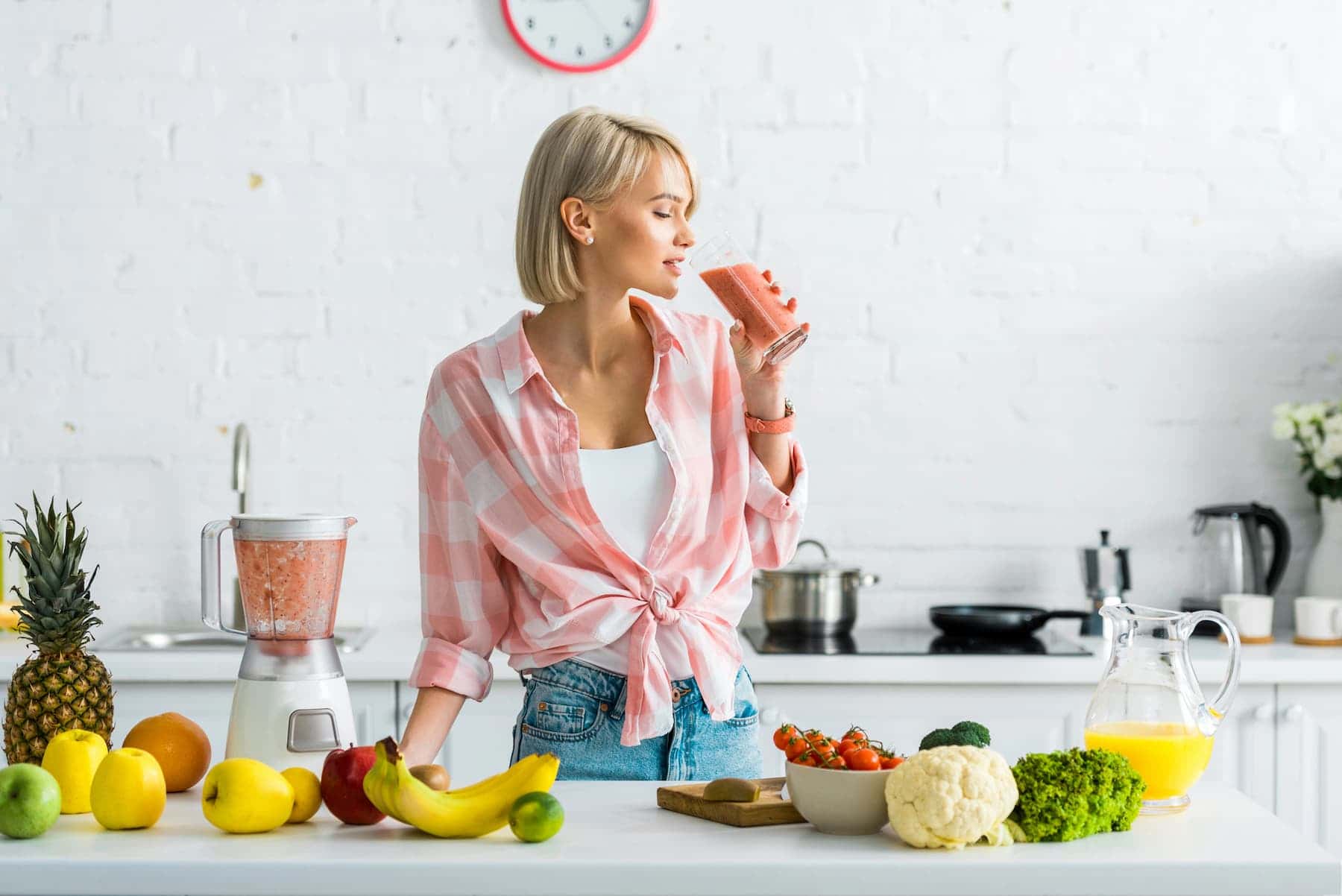 A tall and slim woman drinks smoothie in her kitchen.