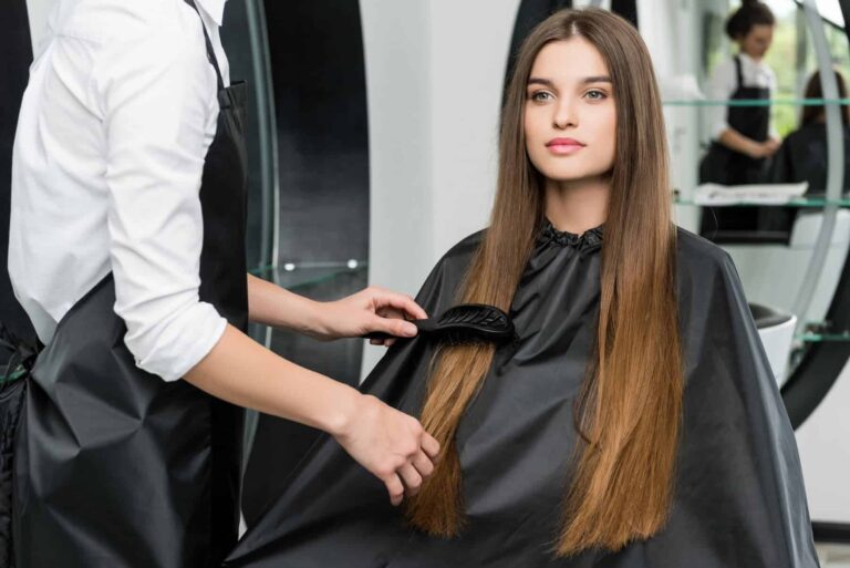 A hairdresser combs a woman’s long brown hair in a salon during a professional hair care appointment.