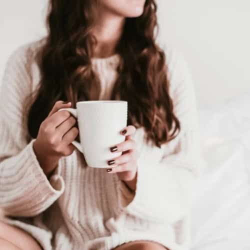 Woman relaxing in bed with a hot beverage.