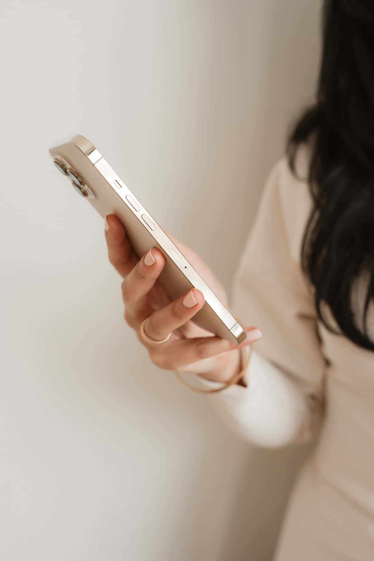 A woman holds a gold smartphone, its side profile highlighted against a soft, neutral background.